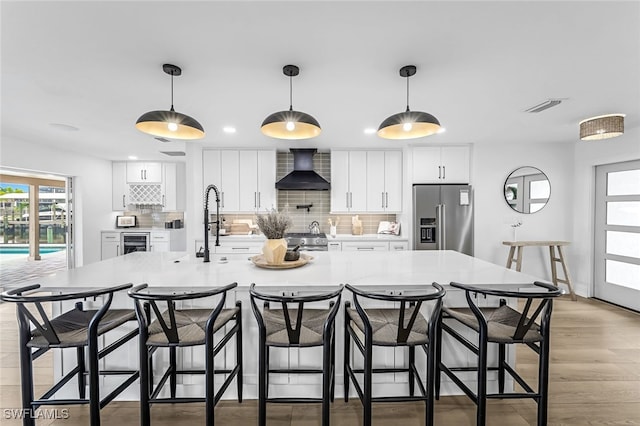 kitchen with decorative backsplash, white cabinetry, stainless steel appliances, and wall chimney range hood