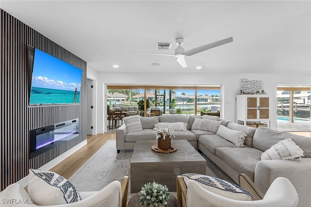 living room featuring ceiling fan, a large fireplace, and light hardwood / wood-style floors