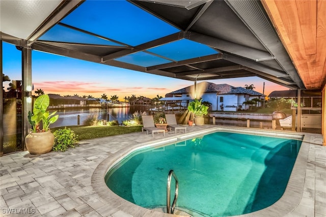 pool at dusk with a lanai, a water view, and a patio