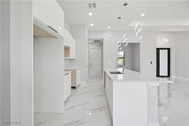 kitchen with white cabinets, sink, decorative light fixtures, and an island with sink