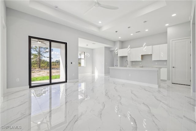 unfurnished living room with a raised ceiling, ceiling fan, and sink