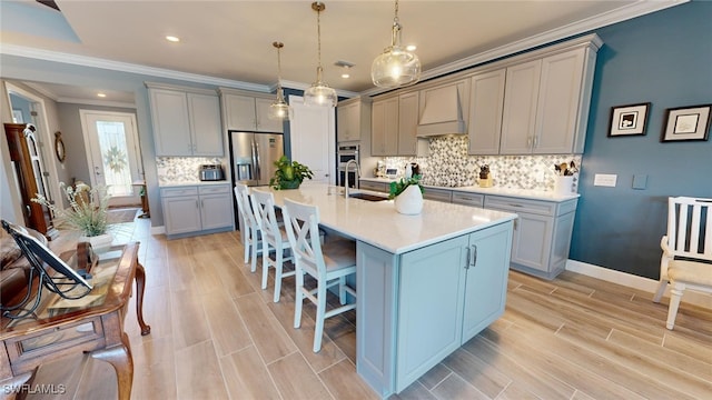 kitchen featuring premium range hood, an island with sink, light hardwood / wood-style floors, and decorative light fixtures