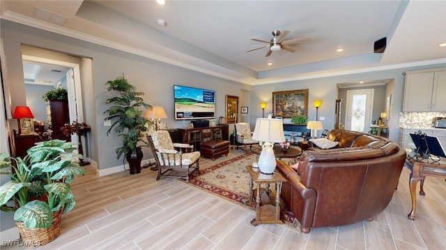 living room featuring light hardwood / wood-style flooring, a raised ceiling, ceiling fan, and ornamental molding