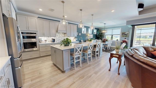 kitchen with premium range hood, pendant lighting, a breakfast bar area, a kitchen island with sink, and appliances with stainless steel finishes