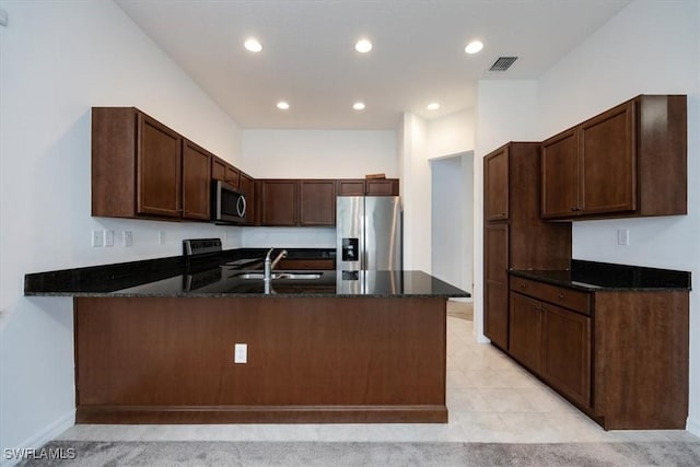 kitchen featuring dark brown cabinetry, sink, kitchen peninsula, dark stone countertops, and appliances with stainless steel finishes