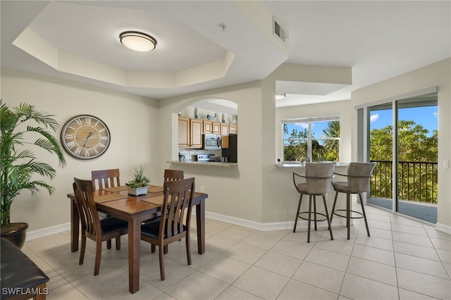 dining room featuring light tile patterned floors, visible vents, a tray ceiling, and baseboards