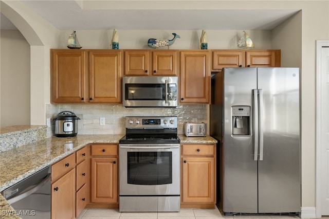 kitchen featuring light stone countertops, light tile patterned floors, appliances with stainless steel finishes, and decorative backsplash