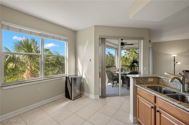 kitchen featuring baseboards, brown cabinets, light stone countertops, a sink, and light tile patterned flooring