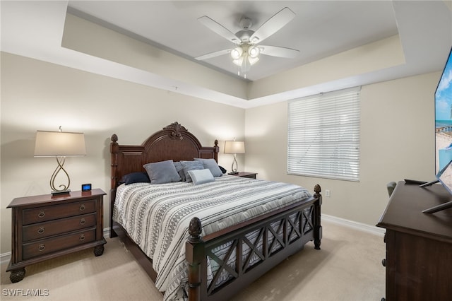 bedroom featuring a raised ceiling, light colored carpet, ceiling fan, and baseboards