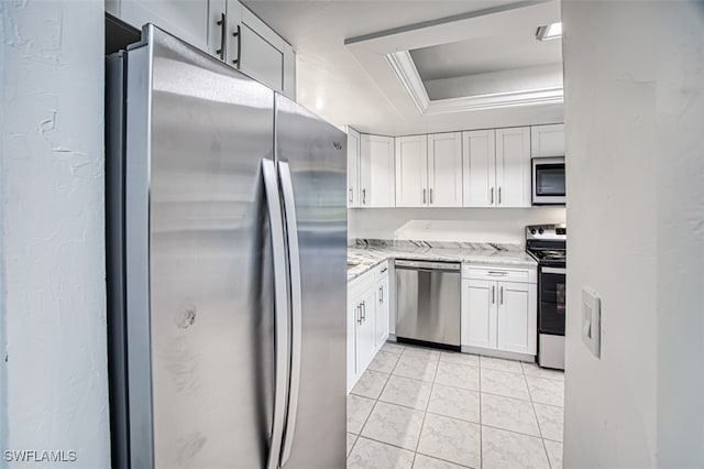 kitchen with light stone counters, stainless steel appliances, a raised ceiling, white cabinetry, and light tile patterned flooring