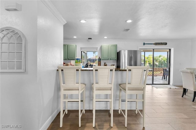 kitchen with green cabinets, ornamental molding, stainless steel fridge, a breakfast bar area, and hardwood / wood-style flooring