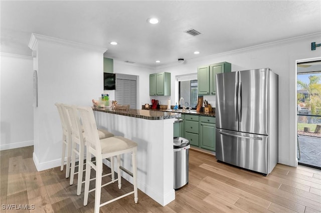 kitchen featuring sink, kitchen peninsula, stainless steel fridge, a breakfast bar area, and green cabinetry