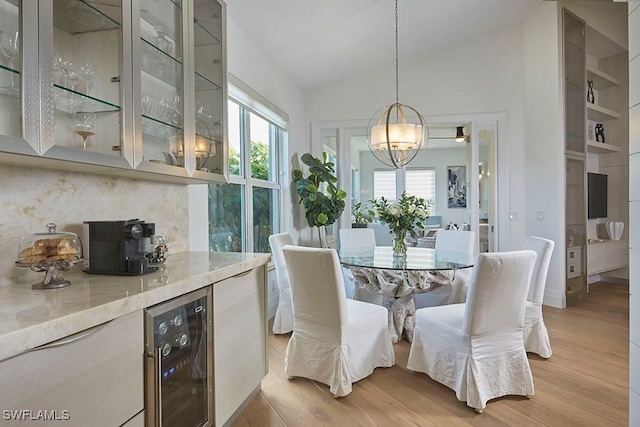 dining space featuring lofted ceiling, light hardwood / wood-style flooring, beverage cooler, and a chandelier