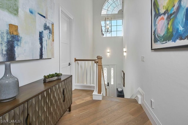 foyer entrance with a towering ceiling, wood-type flooring, and a chandelier