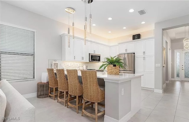 kitchen featuring a kitchen bar, appliances with stainless steel finishes, decorative backsplash, pendant lighting, and white cabinets