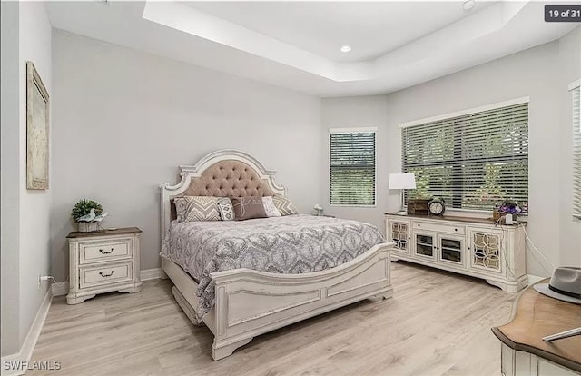 bedroom with a raised ceiling and light wood-type flooring