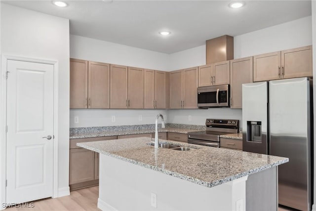 kitchen featuring light stone counters, stainless steel appliances, sink, a center island with sink, and light hardwood / wood-style flooring