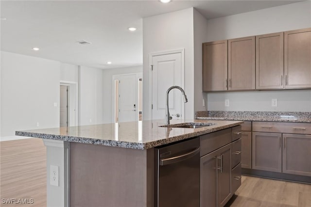 kitchen featuring light stone counters, stainless steel dishwasher, a kitchen island with sink, sink, and light hardwood / wood-style flooring