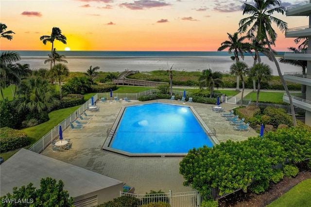 pool at dusk featuring a patio area and a water view