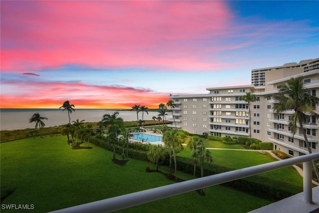 pool at dusk with a water view and a lawn