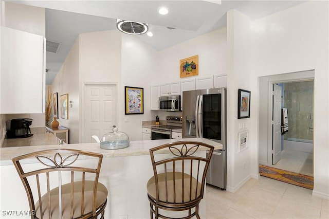 kitchen with a high ceiling, light tile patterned floors, white cabinetry, kitchen peninsula, and stainless steel appliances