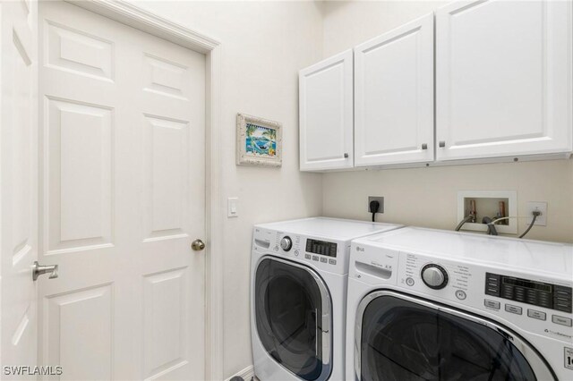 clothes washing area with washing machine and clothes dryer and cabinets