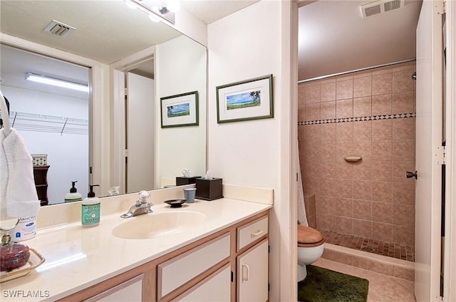 bathroom featuring tile patterned floors, vanity, toilet, and a tile shower