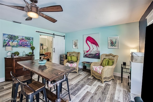 dining room with ceiling fan, a barn door, and wood-type flooring