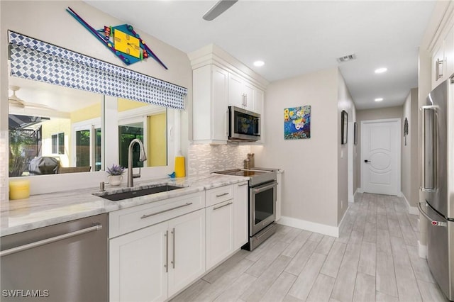 kitchen with light stone countertops, appliances with stainless steel finishes, backsplash, sink, and white cabinetry