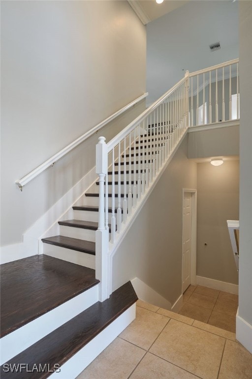 stairway with visible vents, tile patterned flooring, a towering ceiling, and baseboards