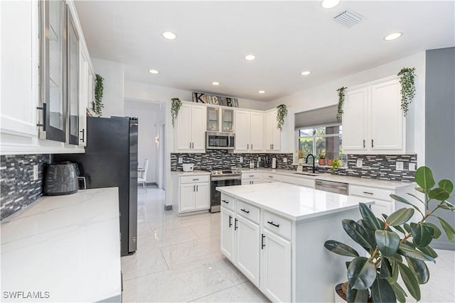 kitchen featuring white cabinets, sink, light stone countertops, a kitchen island, and stainless steel appliances