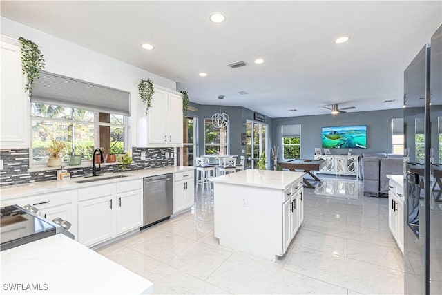 kitchen with stainless steel dishwasher, a kitchen island, white cabinets, and sink