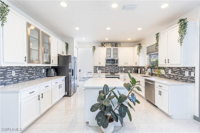 kitchen with sink, decorative backsplash, appliances with stainless steel finishes, a kitchen island, and white cabinetry