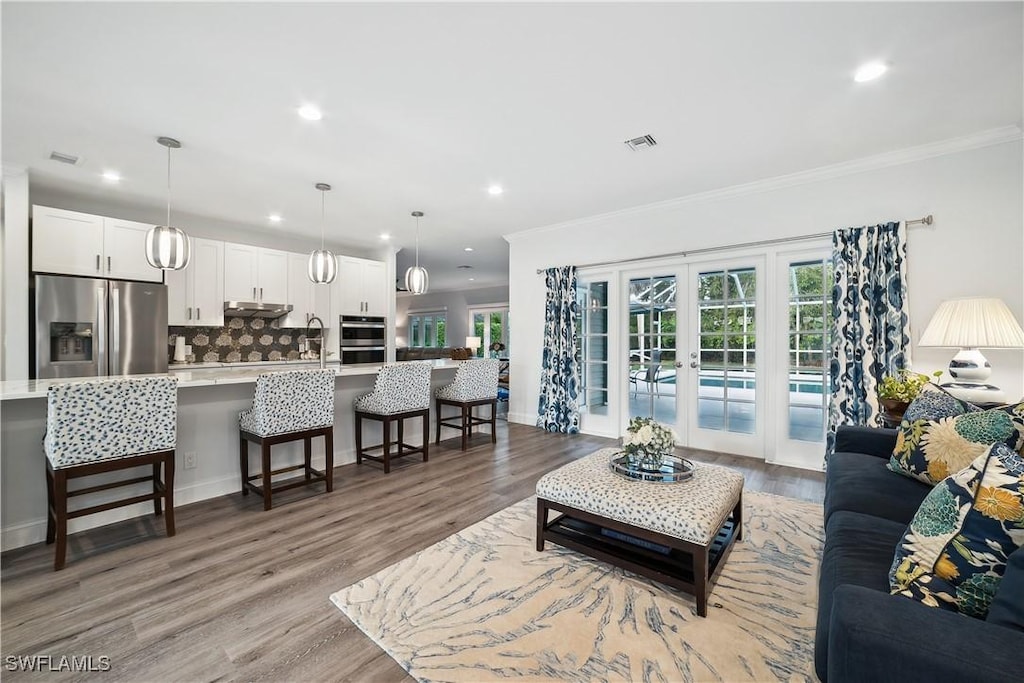 living room with crown molding, light wood-type flooring, and french doors