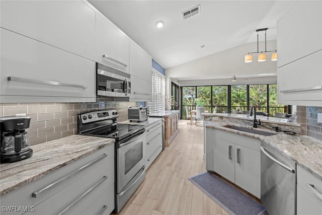 kitchen featuring sink, hanging light fixtures, lofted ceiling, white cabinets, and appliances with stainless steel finishes