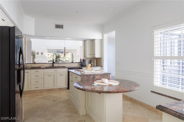 kitchen featuring sink, a center island, ornamental molding, black fridge with ice dispenser, and cream cabinetry