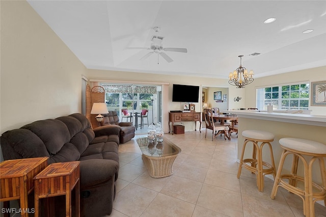 living room with ceiling fan with notable chandelier, a raised ceiling, and light tile patterned floors