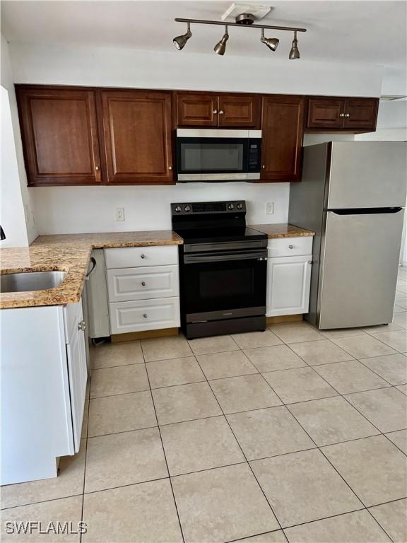 kitchen with sink, white cabinetry, light stone counters, light tile patterned floors, and appliances with stainless steel finishes