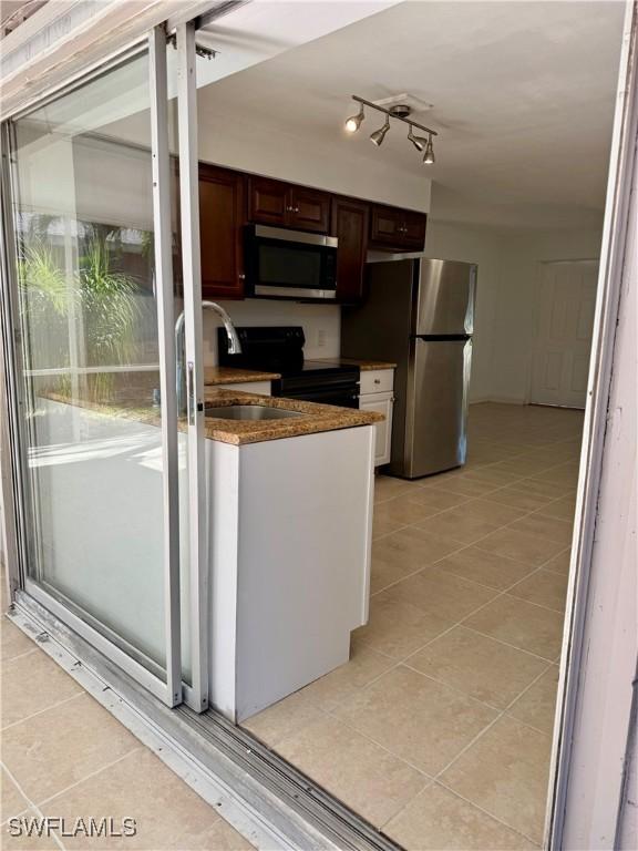 kitchen with stainless steel appliances, sink, light tile patterned floors, and dark brown cabinetry