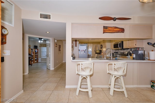 kitchen featuring appliances with stainless steel finishes, a kitchen bar, decorative backsplash, kitchen peninsula, and light brown cabinets