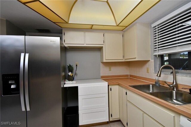 kitchen featuring decorative backsplash, stainless steel fridge, white cabinetry, and sink