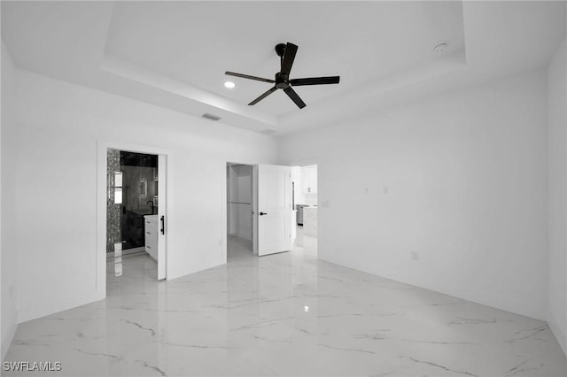 empty room with ceiling fan and a raised ceiling