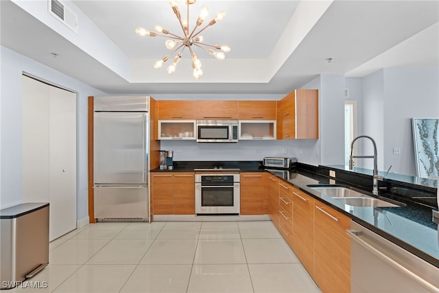 kitchen with sink, stainless steel appliances, dark stone countertops, a chandelier, and a tray ceiling