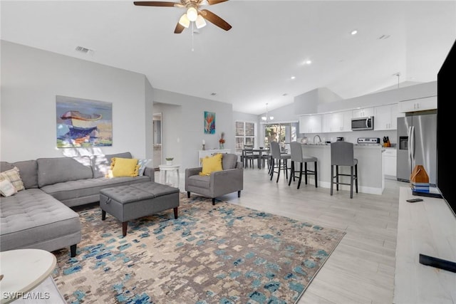 living room featuring sink, ceiling fan with notable chandelier, lofted ceiling, and light wood-type flooring