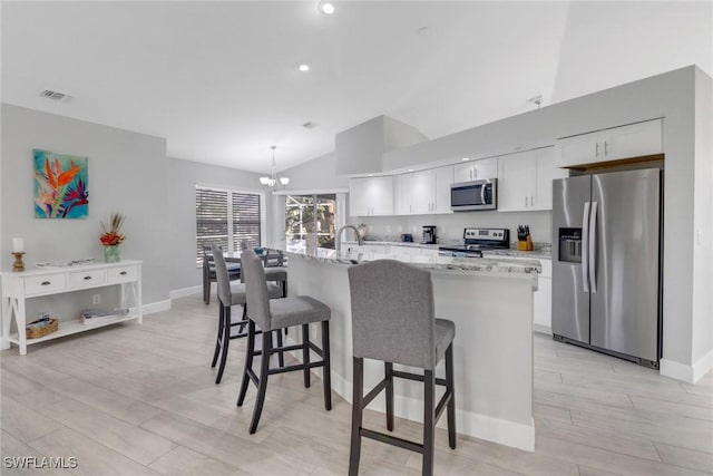 kitchen featuring stainless steel appliances, decorative light fixtures, light hardwood / wood-style floors, white cabinetry, and an island with sink