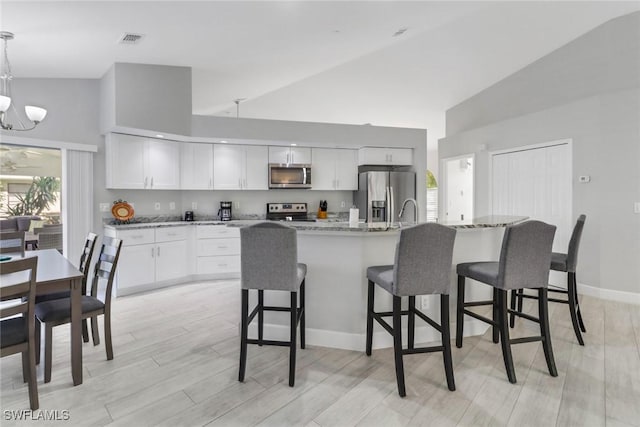 kitchen with light stone countertops, appliances with stainless steel finishes, high vaulted ceiling, white cabinets, and hanging light fixtures