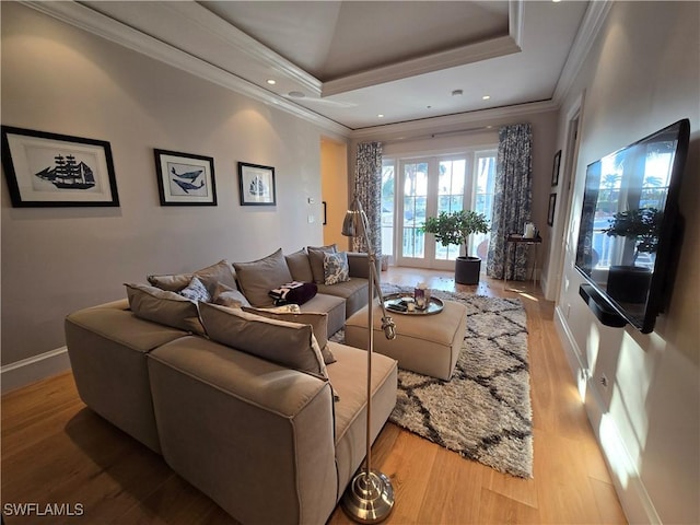 living room with a raised ceiling, crown molding, and light wood-style flooring