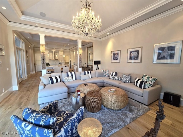 living area featuring a chandelier, a tray ceiling, crown molding, and light wood-style floors