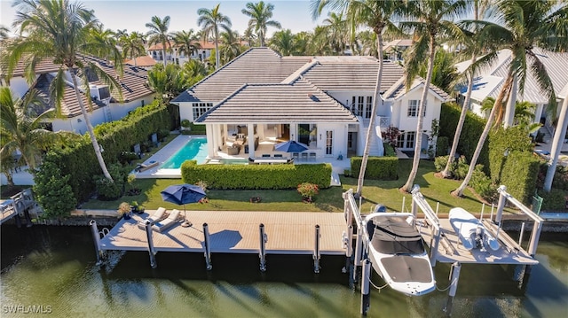 back of house with a patio, boat lift, a water view, a tiled roof, and an outdoor pool