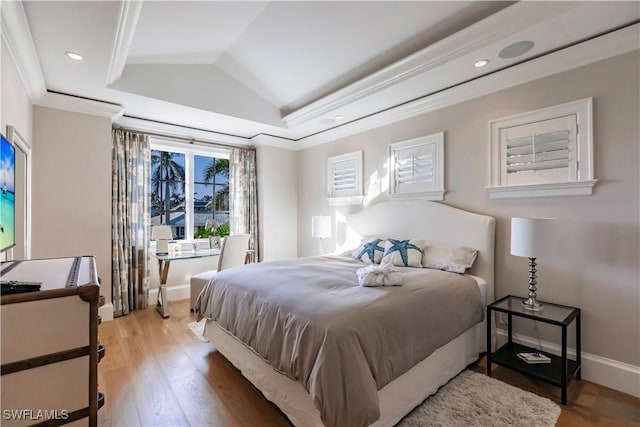 bedroom featuring lofted ceiling, baseboards, light wood-type flooring, a raised ceiling, and crown molding